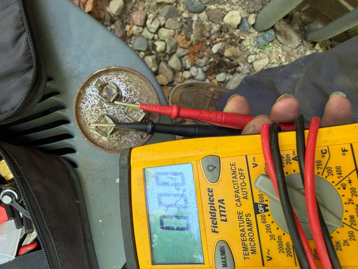 Multimeter testing a capacitor on an outdoor AC condenser