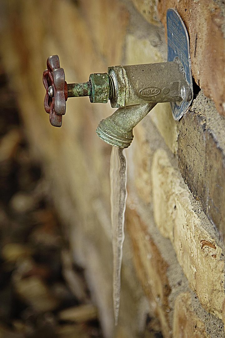 Frozen outdoor faucet with an icicle on a brick house wall