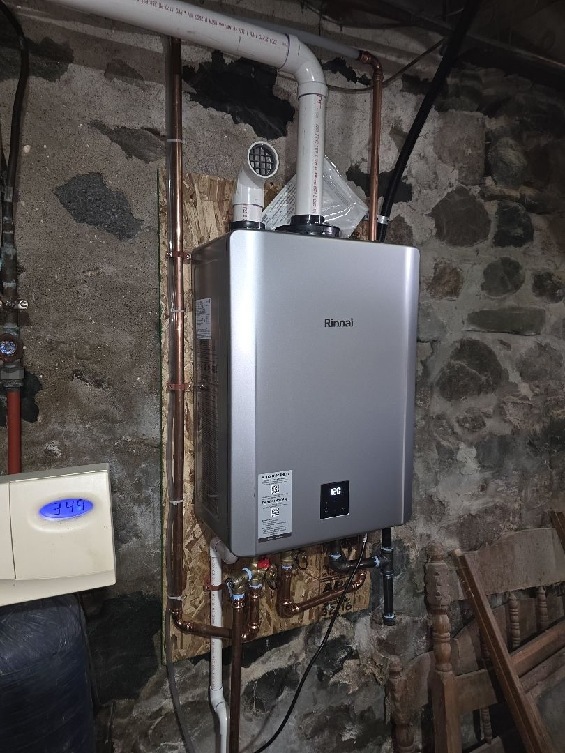 Rinnai tankless water heater on a stone basement wall with white vent piping and copper lines