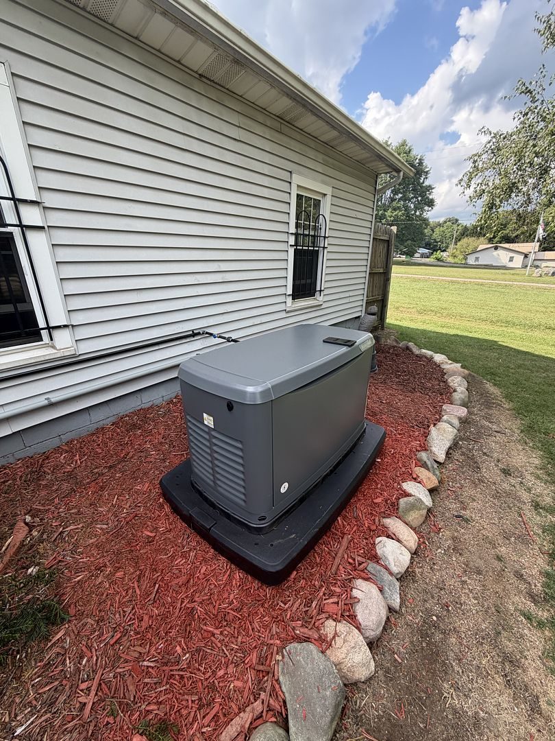 New standby generator on a pad beside the home, finished with a red mulch and stone border