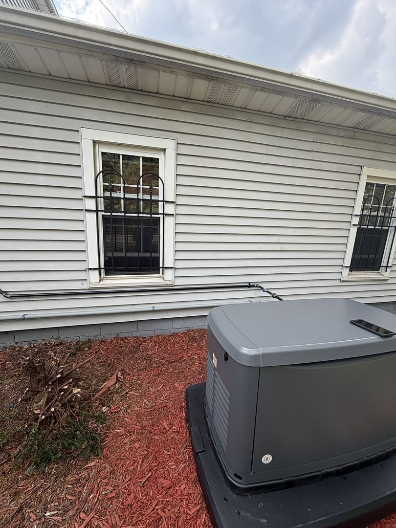 Standby generator on its pad next to the siding and window of the home